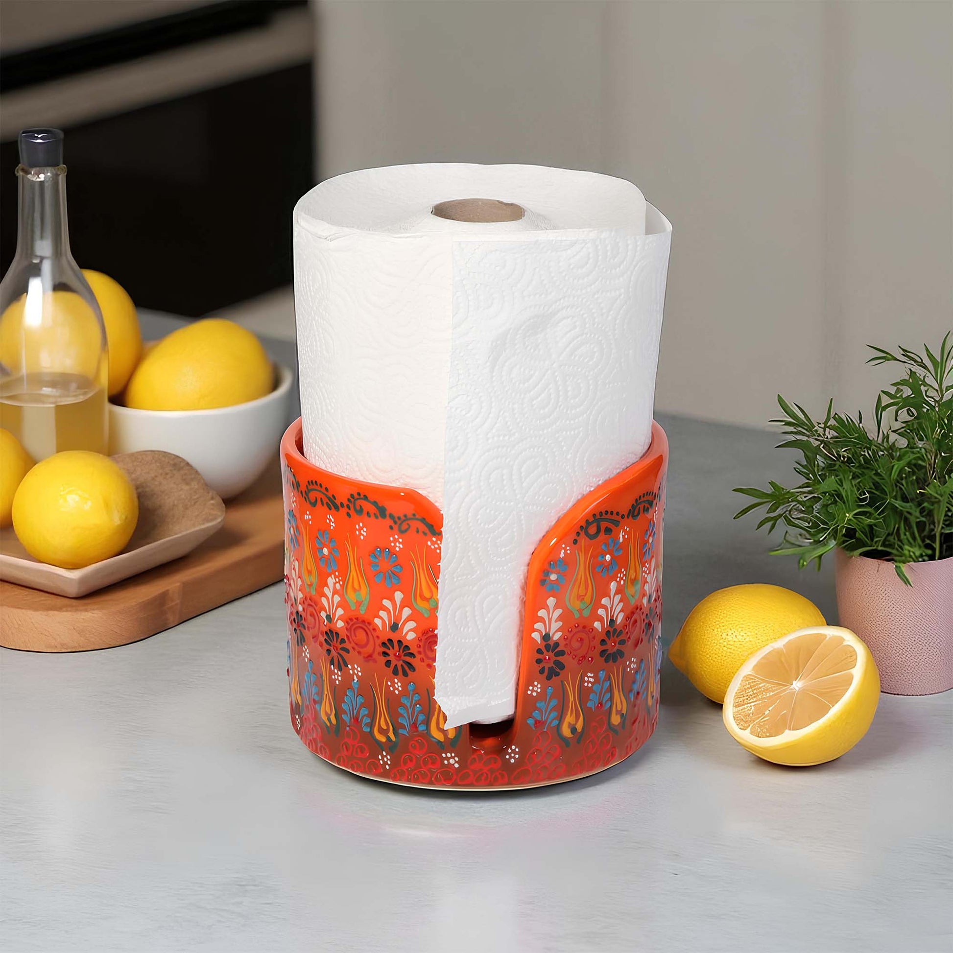 Decorative paper towel holder with a roll of paper towels on a kitchen counter with lemons and a plant.