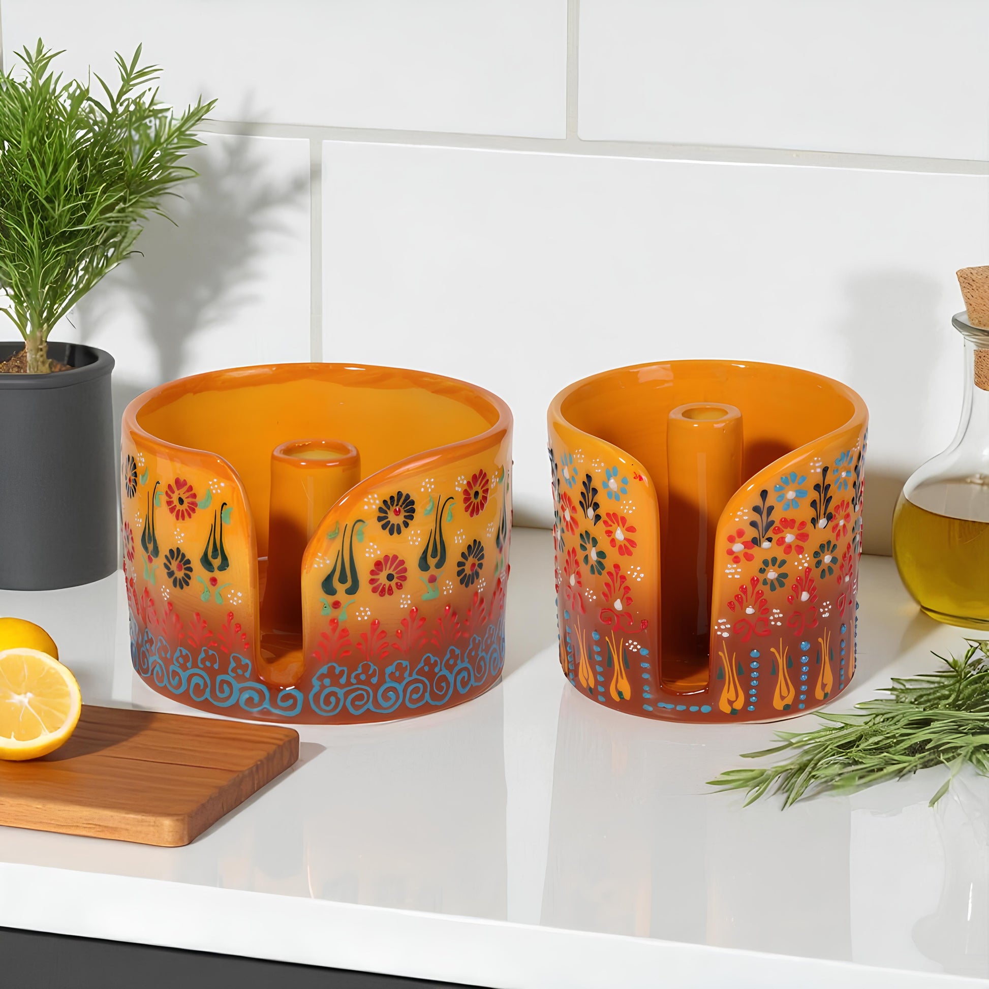 Two decorative orange paper towel holders with floral designs on a kitchen counter.