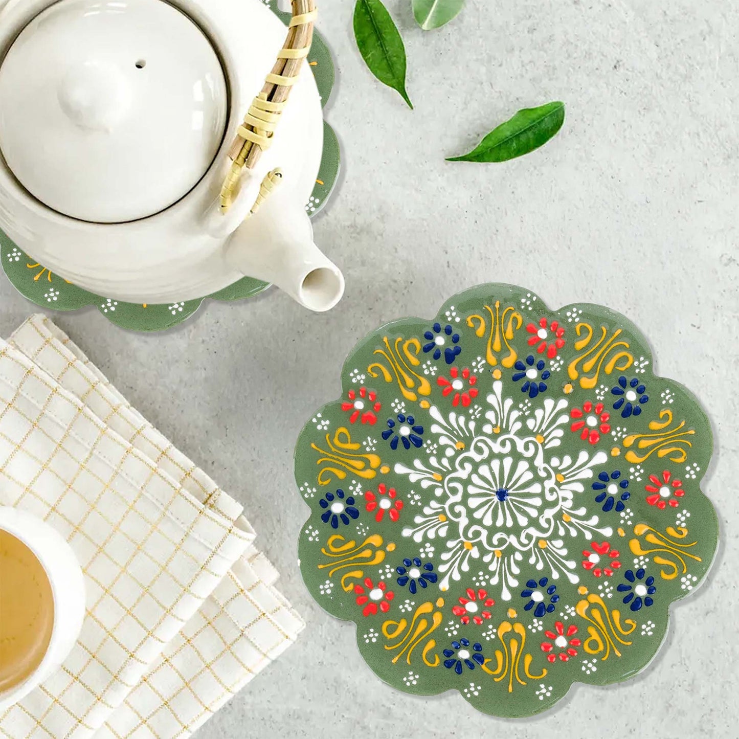Decorative trivet with floral pattern on a table with a teapot and cup.