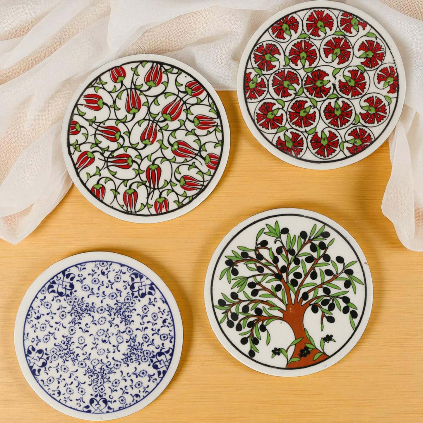 Set of four ceramic coasters with floral and nature-themed designs on a wooden surface.
