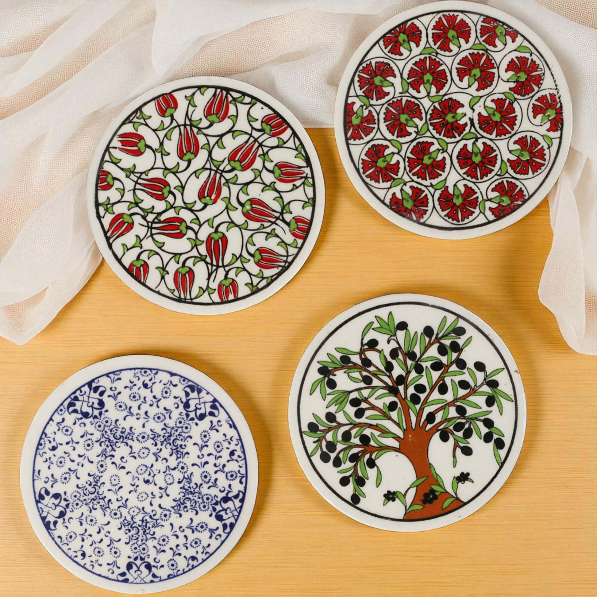 Set of four ceramic coasters with floral and nature-themed designs on a wooden surface.