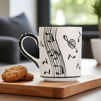 White mug with black musical notes on a wooden surface with cookies