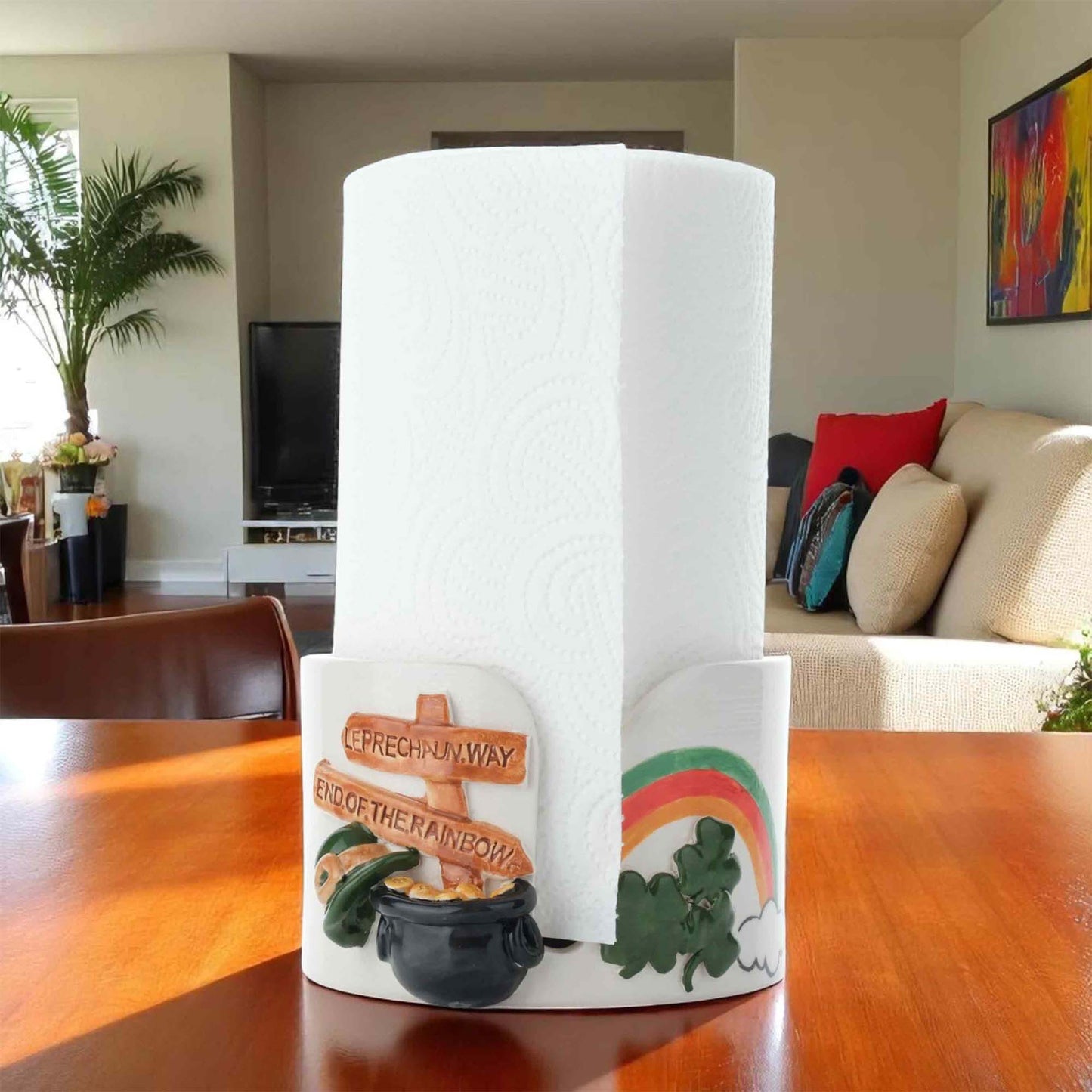 Paper towel roll with a decorative paper towel holder featuring a pot of gold and rainbow design on a wooden table.