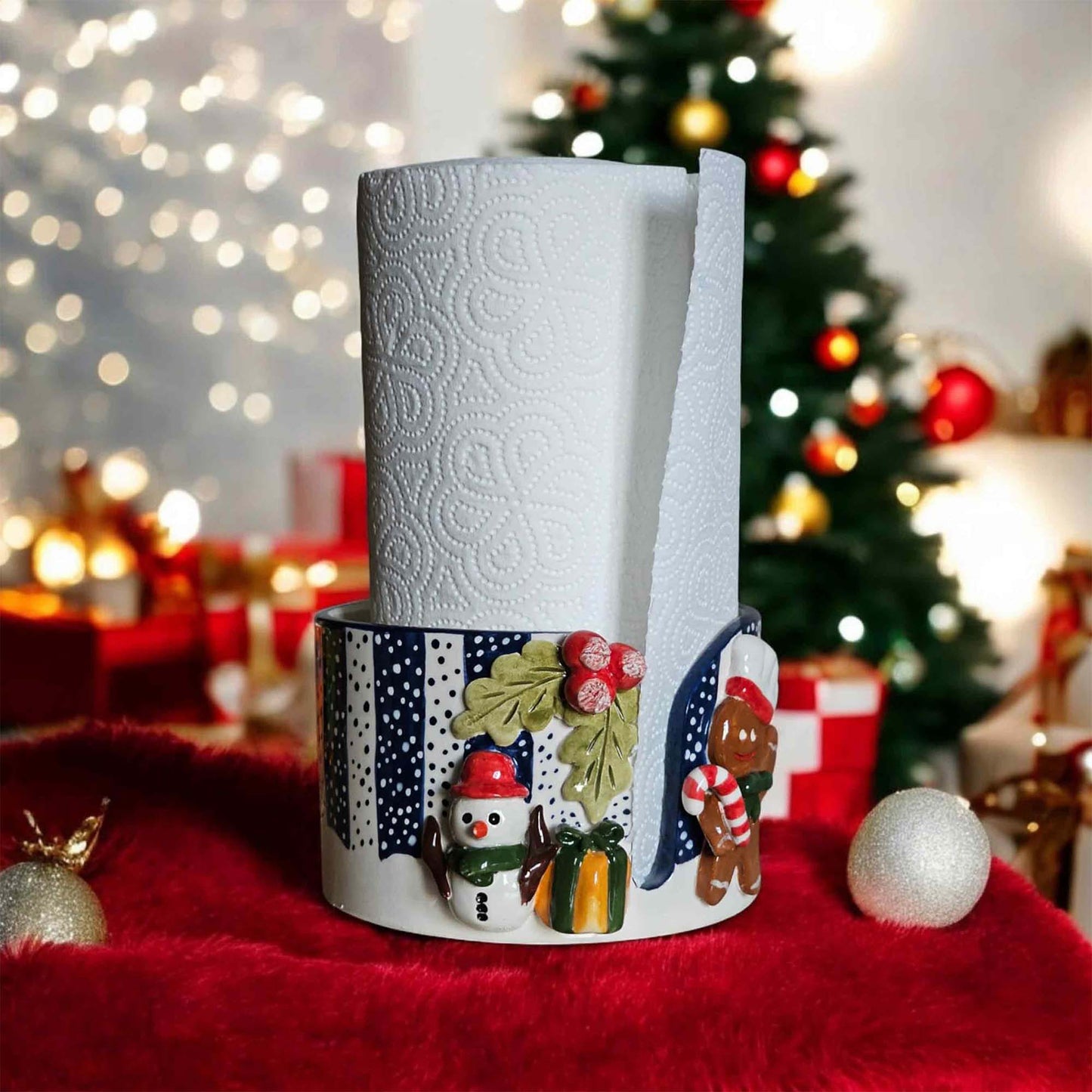 Decorative paper towel holder with Christmas design on a red surface with a blurred festive background.
