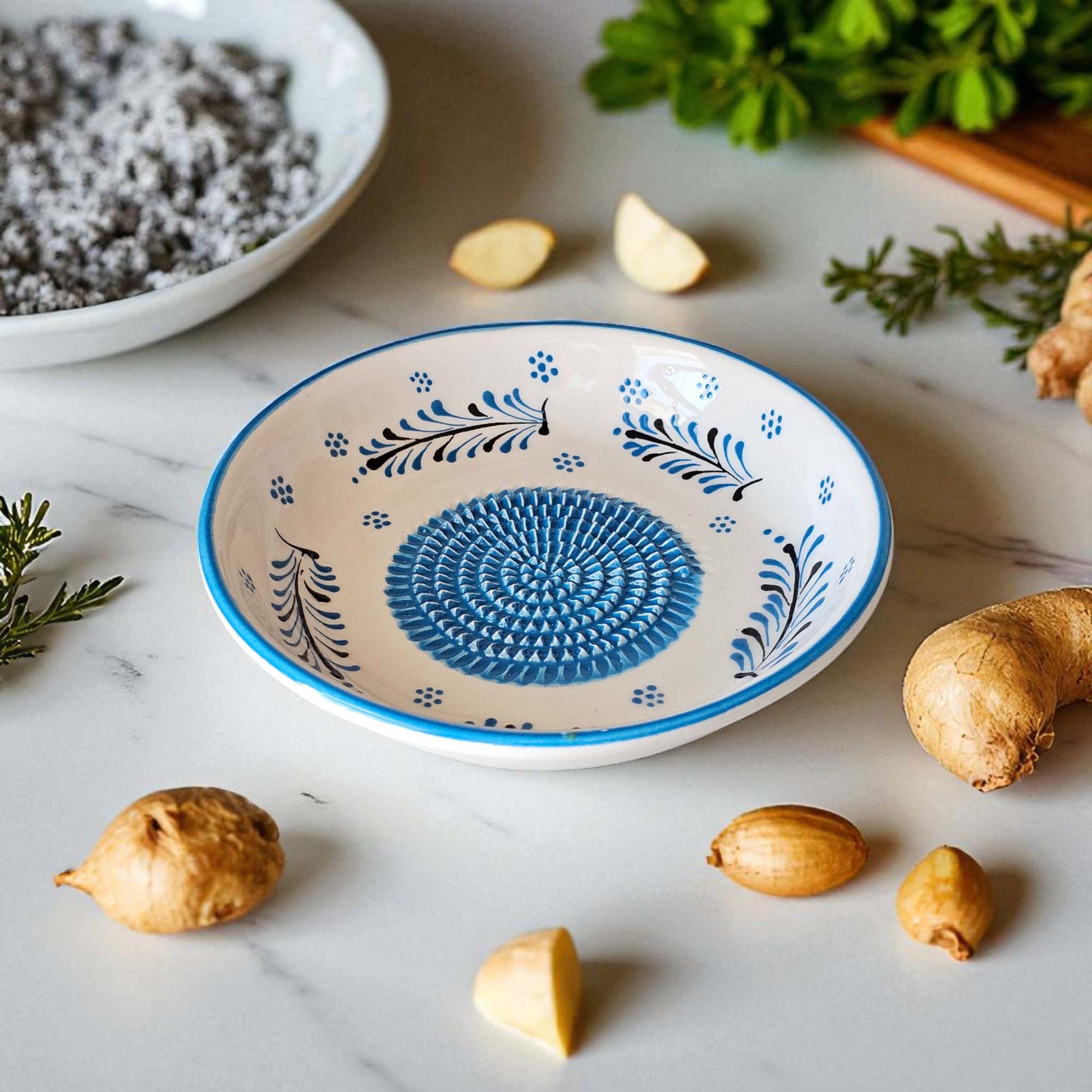 Decorative ceramic garlic grater bowl with blue floral patterns on a marble surface with spices and herbs.