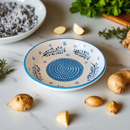 Decorative ceramic garlic grater bowl with blue floral patterns on a marble surface with spices and herbs.