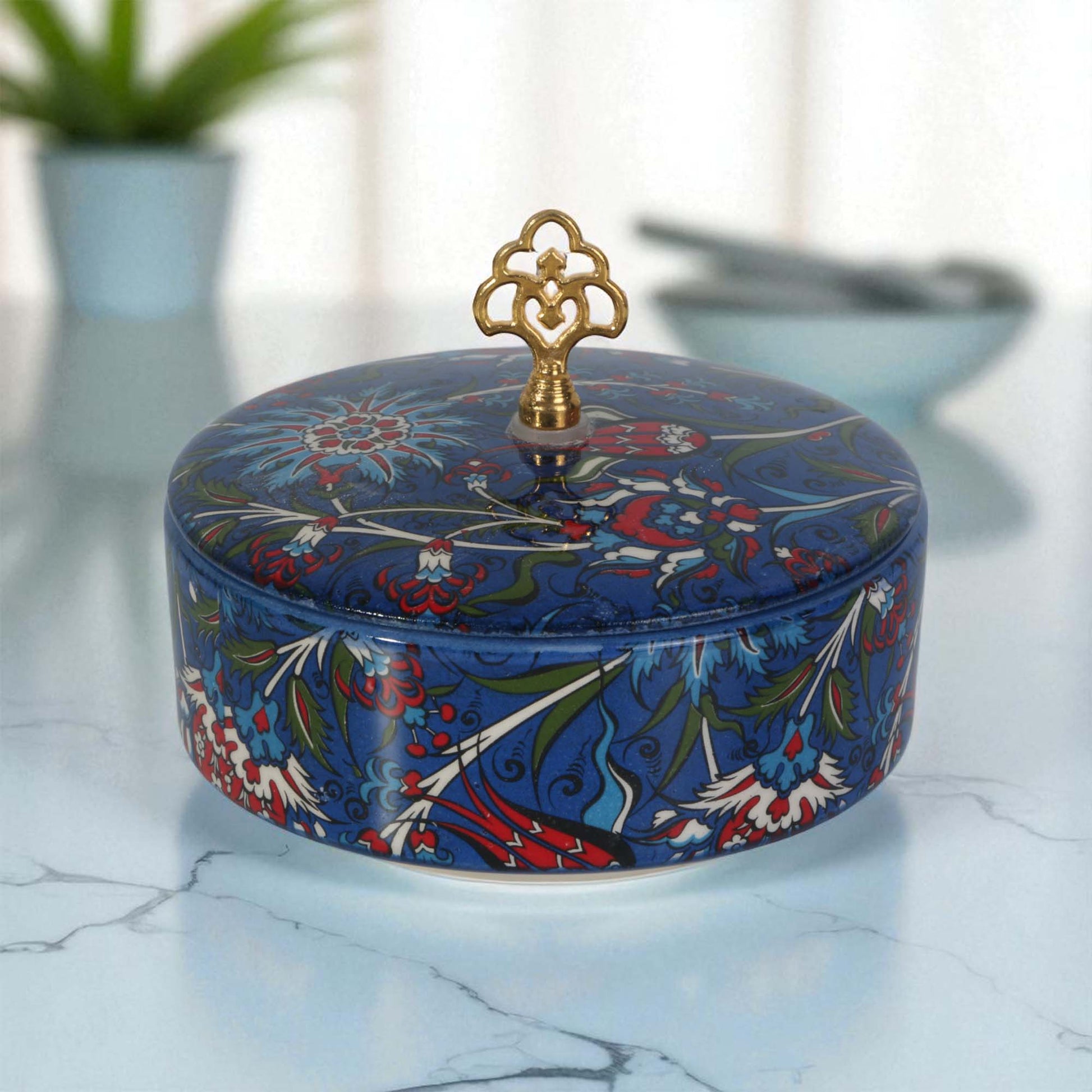 Decorative blue sugar bowl with floral patterns and a gold lid on a marble surface.