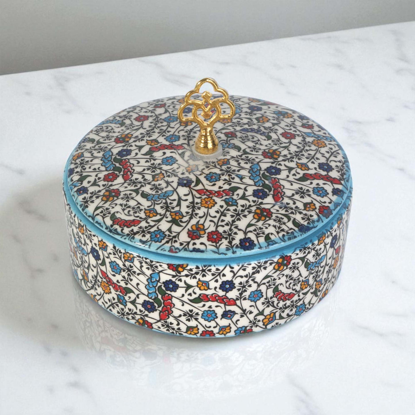 Round decorative sugar bowl with floral pattern and gold lid on a marble surface