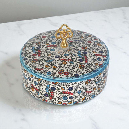 Round decorative sugar bowl with floral pattern and gold lid on a marble surface