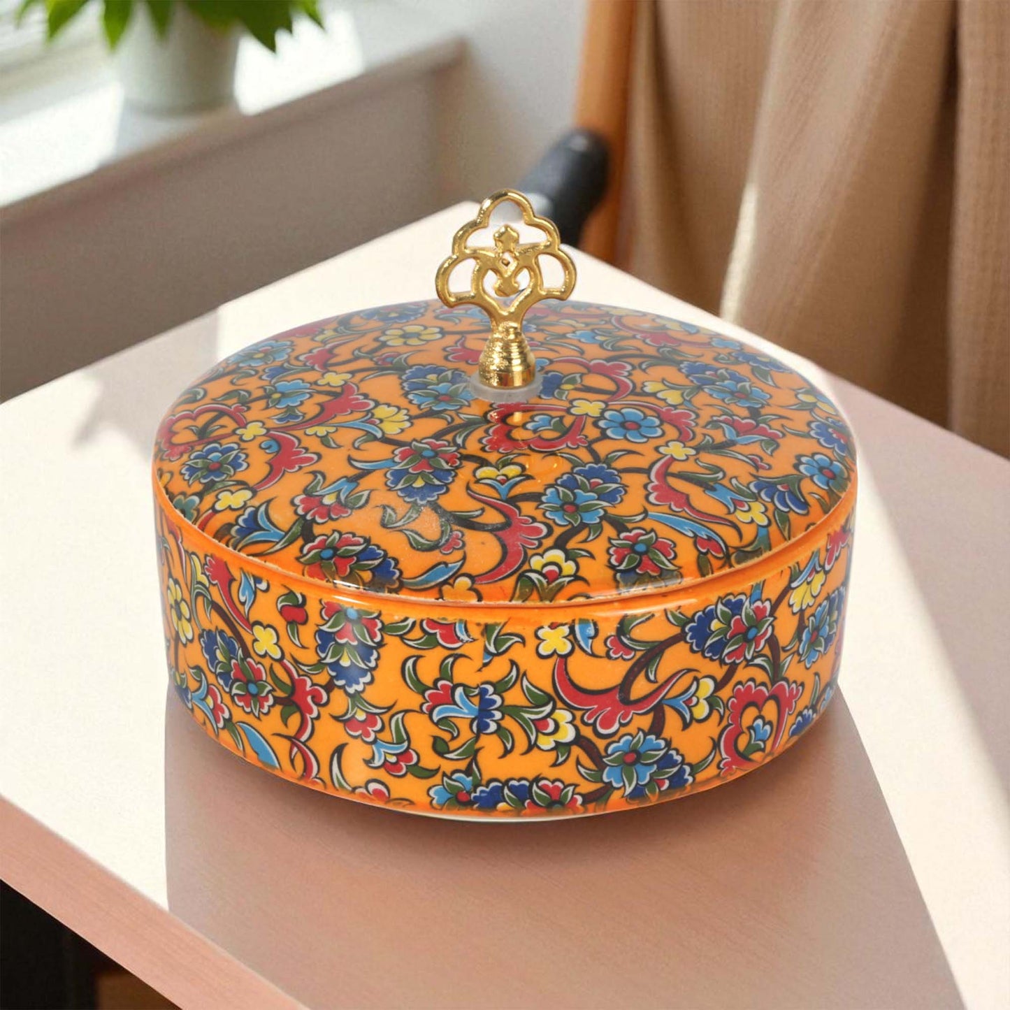 Decorative sugar bowl with floral patterns and a gold lid on a light surface.