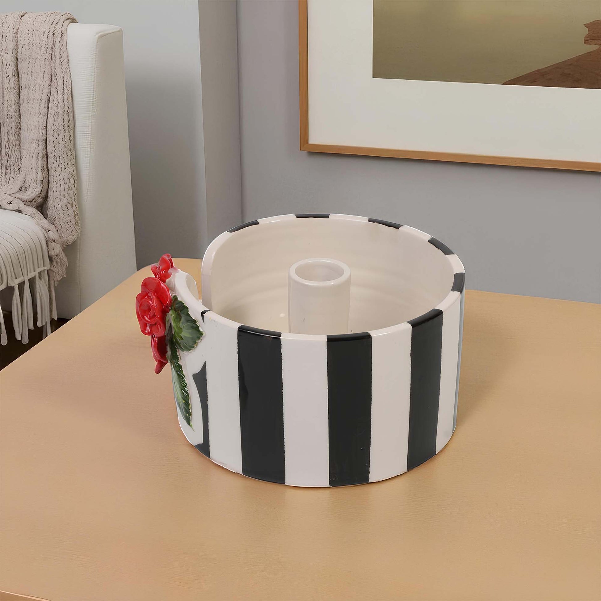 Black and white striped paper towel holder with a red flower on a beige surface