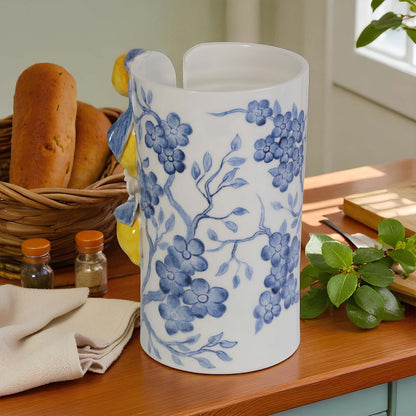 White paper towel holder with blue floral patterns on a wooden table with bread and kitchen items.