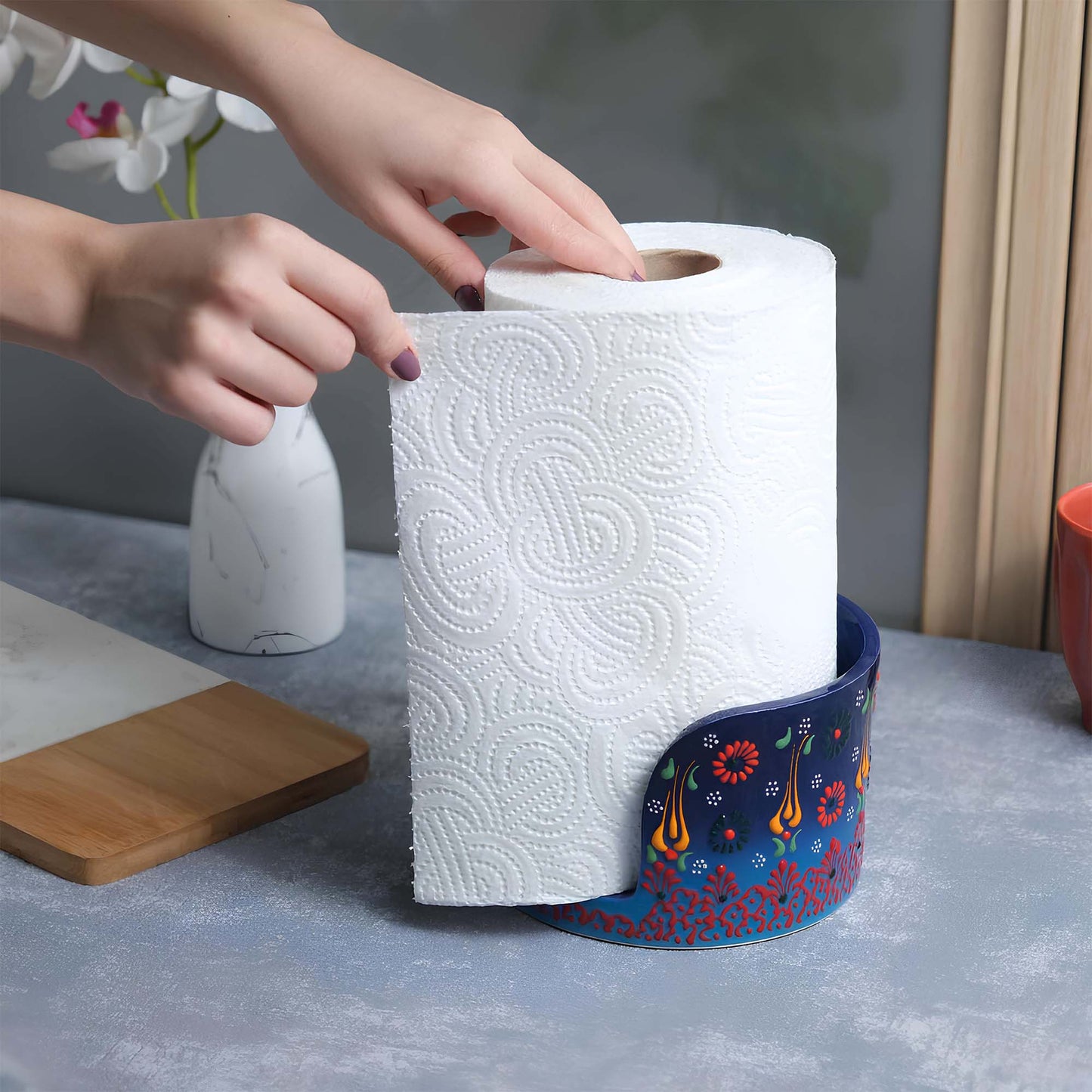 Person reaching for a roll of paper towels in a decorative paper towel holder on a kitchen counter.