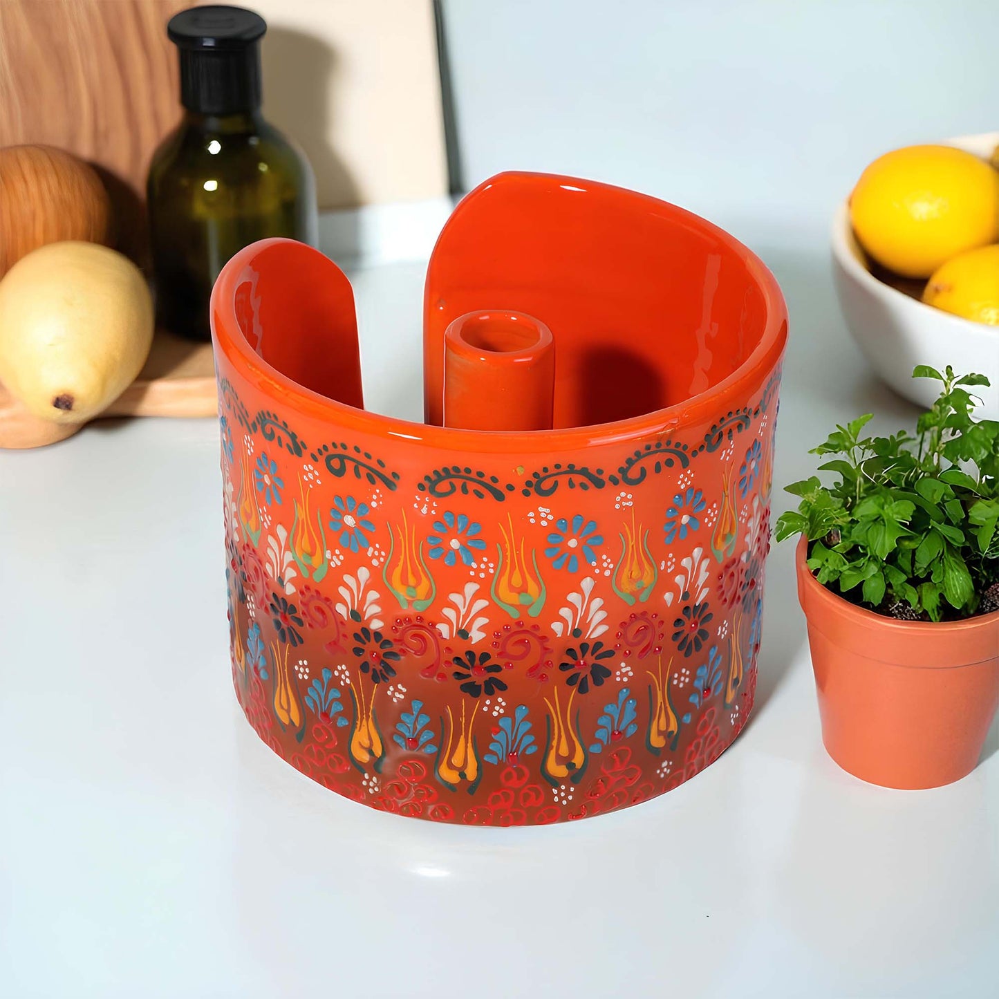 Decorative orange paper towel holder with floral patterns on a white surface with a potted plant and lemons in the background.