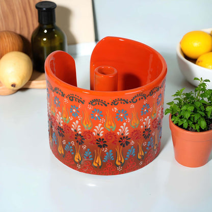 Decorative orange paper towel holder with floral patterns on a white surface with a potted plant and lemons in the background.