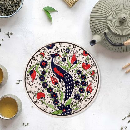 Decorative ceramic trivet with bird and floral design on a white surface with tea-making items.