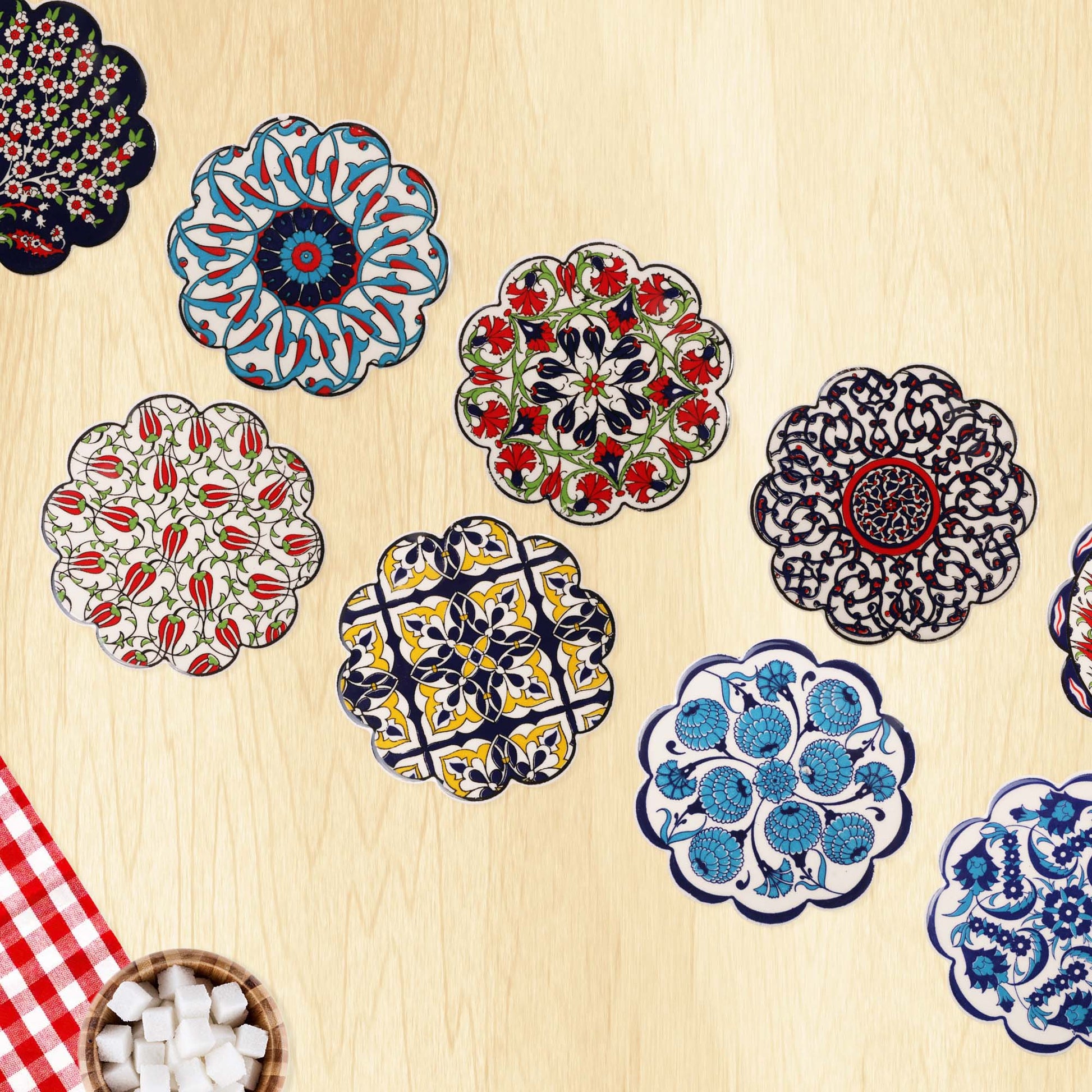 Colorful floral and geometric coasters on a wooden surface with a checkered cloth and bowl of marshmallows.