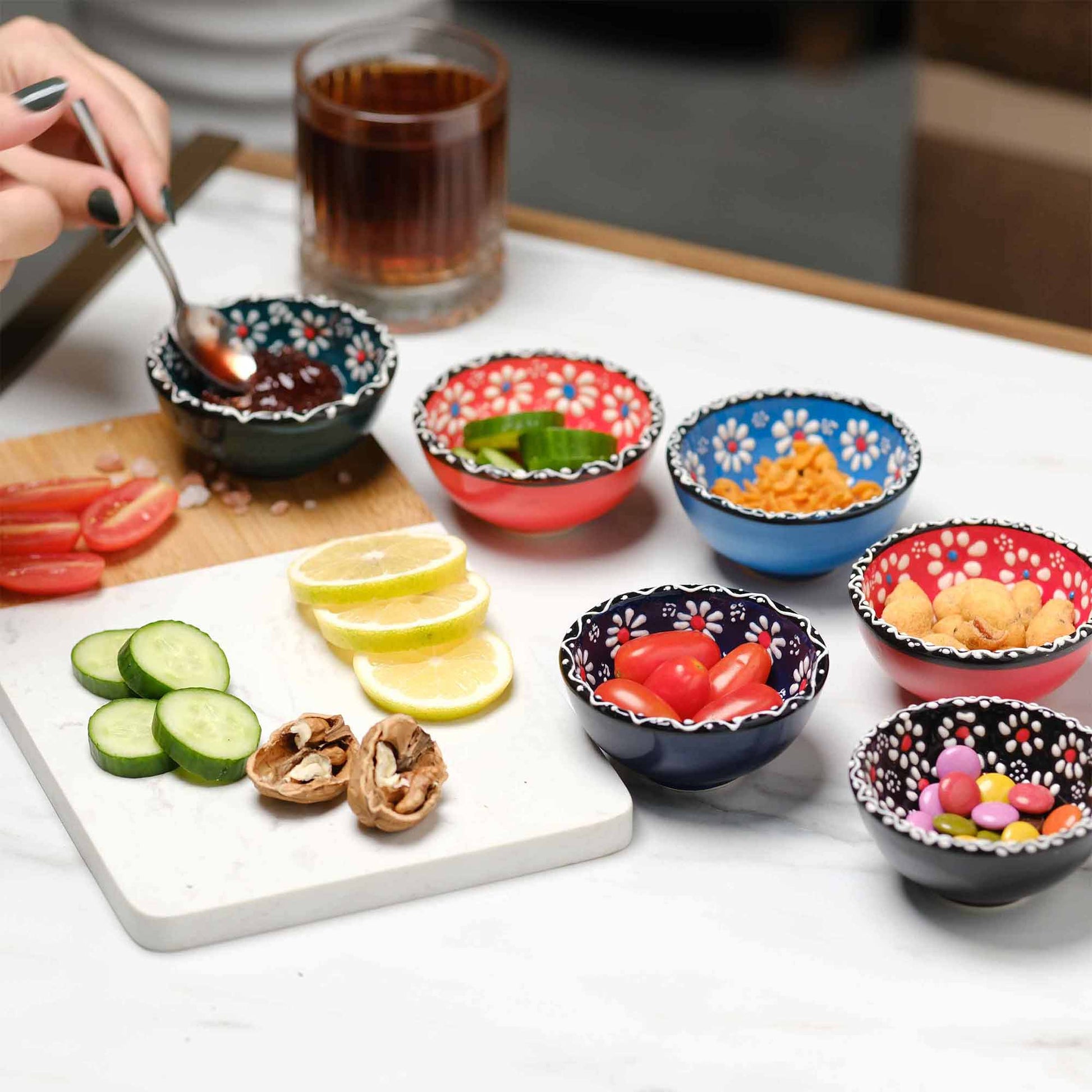 Colorful bowls with snacks on a table with a plate of sliced cucumbers, tomatoes, and lemon.