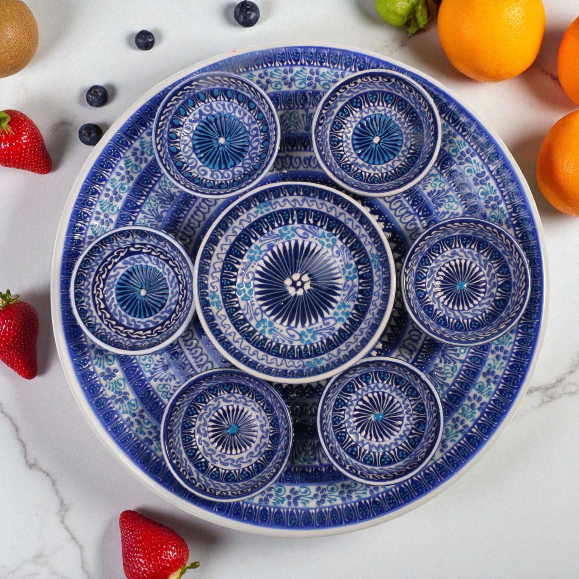 Decorative blue and white plate with intricate patterns on a marble surface with fruits around.