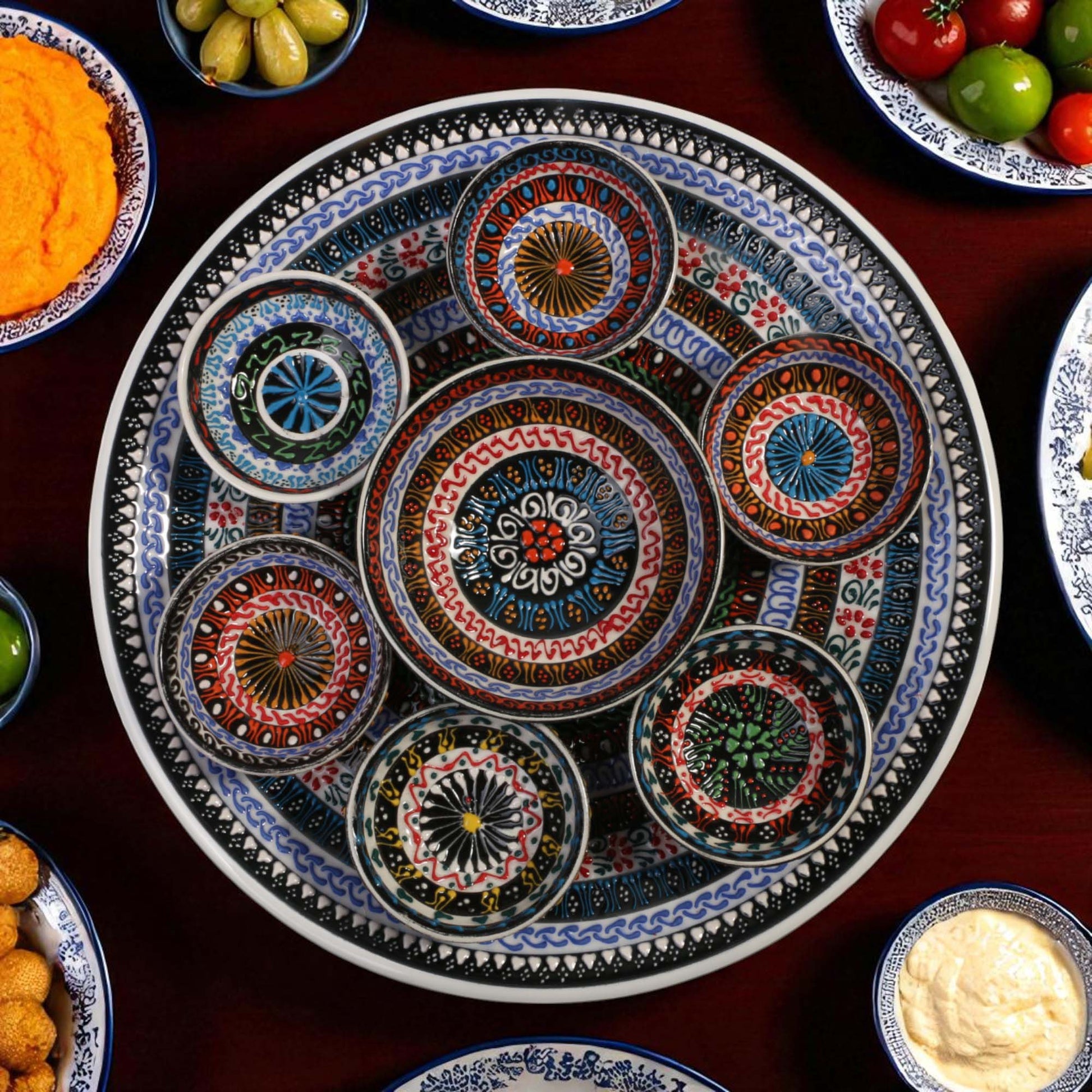 Decorative ceramic plate with side bowls on a table with various food items.
