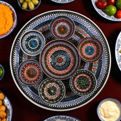 Decorative ceramic plate with side bowls on a table with various food items.