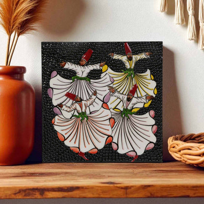 Decorative ceramic wall tile with a dancer design on a black background, placed on a wooden surface.