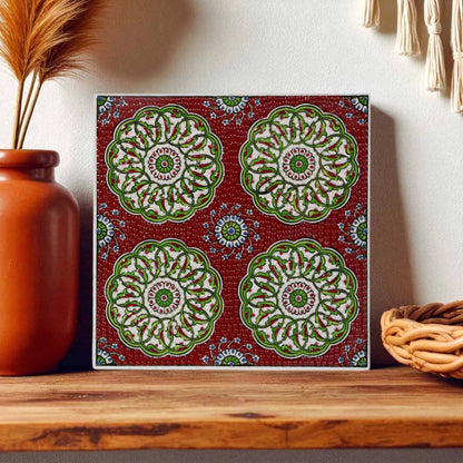 Decorative ceramic tile with green floral patterns on a red background, placed on a wooden surface.