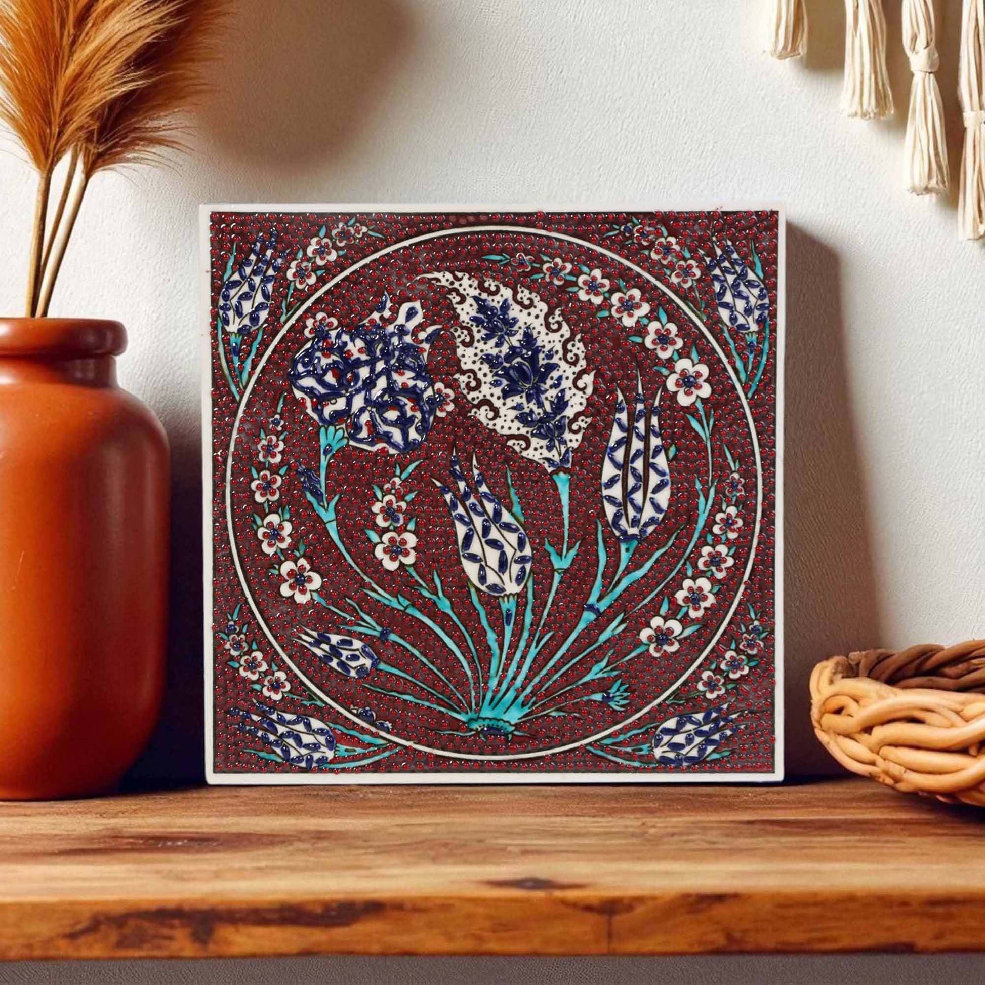 Decorative ceramic tile wall art with floral pattern on a wooden shelf