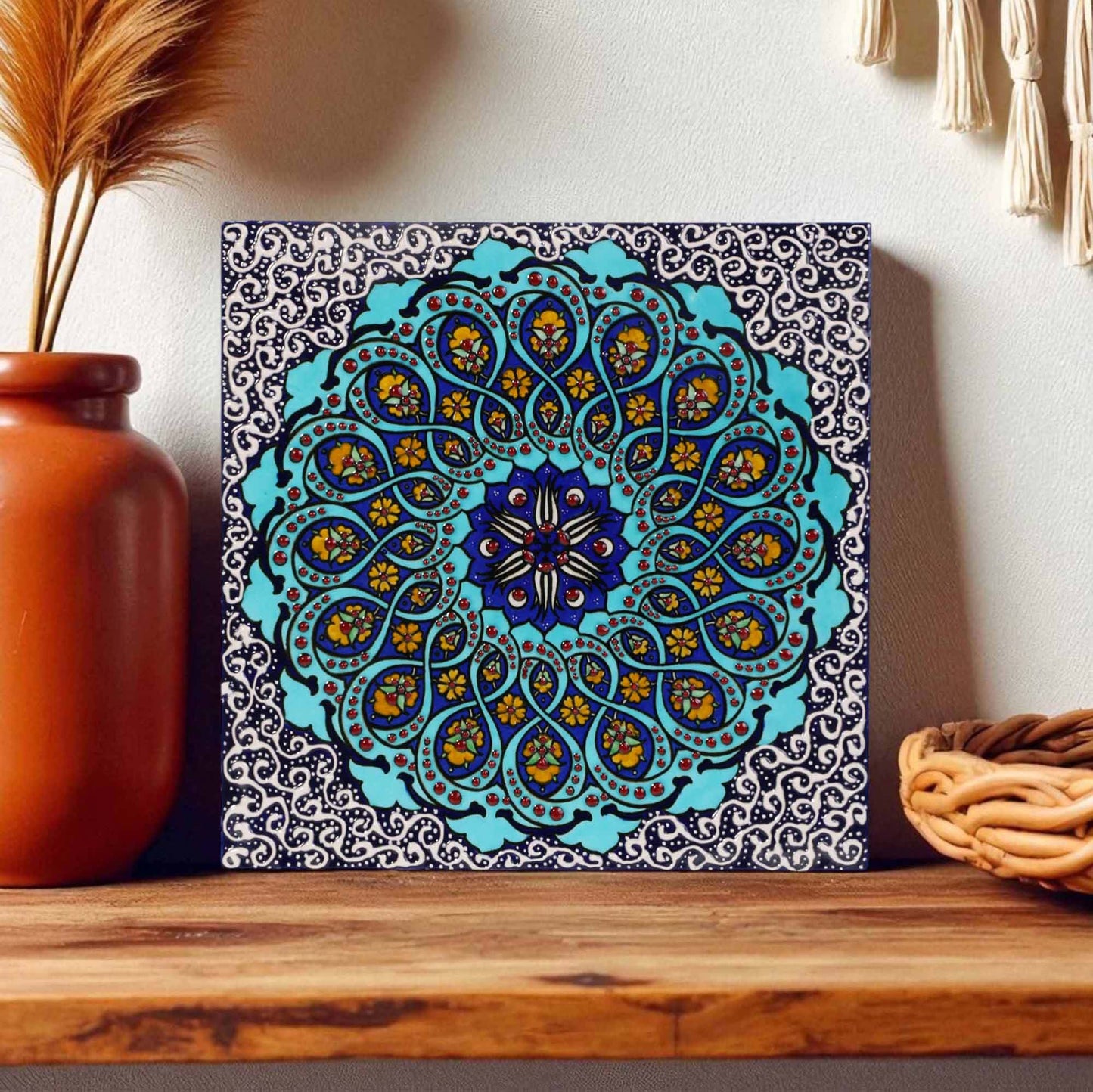 Decorative mandala ceramic tile wall art on a wooden shelf with a vase and basket in the background.