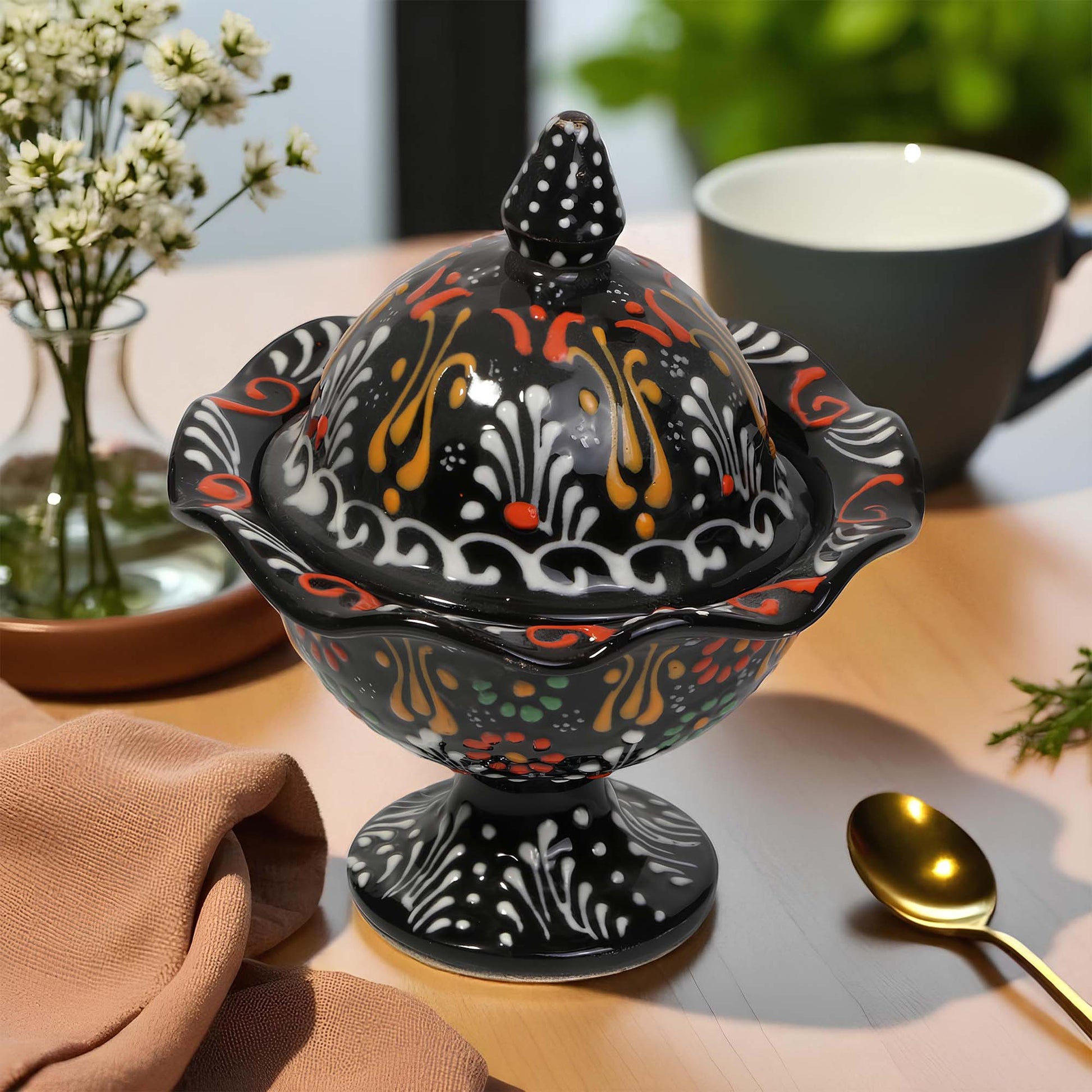 Decorative black sugar bowl with colorful patterns on a table with a cup and spoon.