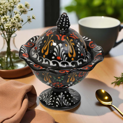 Decorative black sugar bowl with colorful patterns on a table with a cup and spoon.