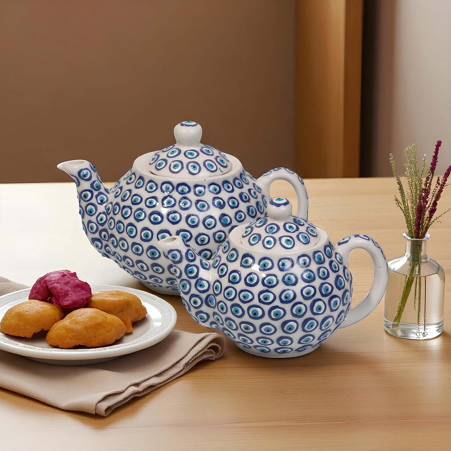 Blue and white patterned teapot on a wooden table with cookies and a vase.