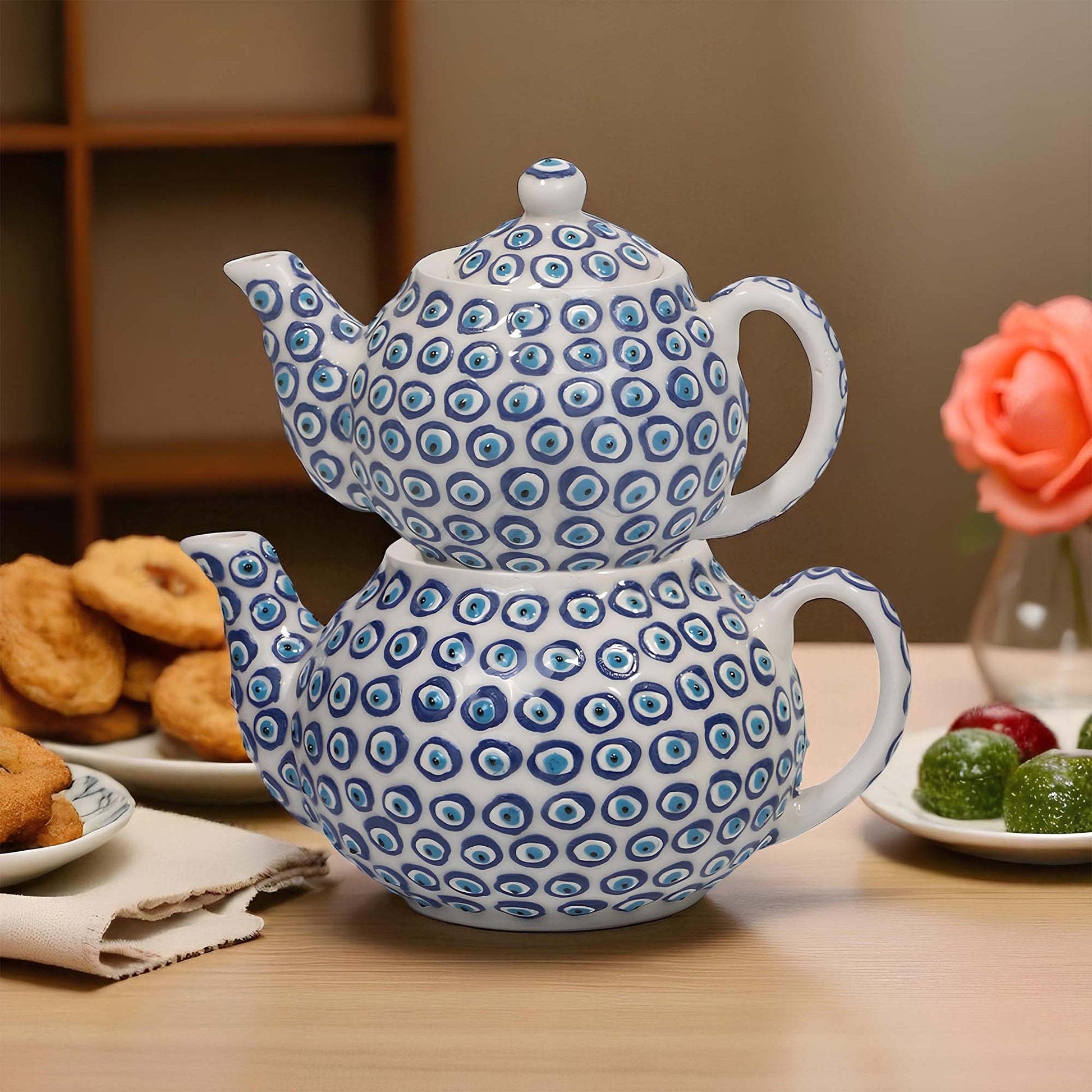 Two stacked ceramic teapots with blue circular pattern on a wooden table with snacks.