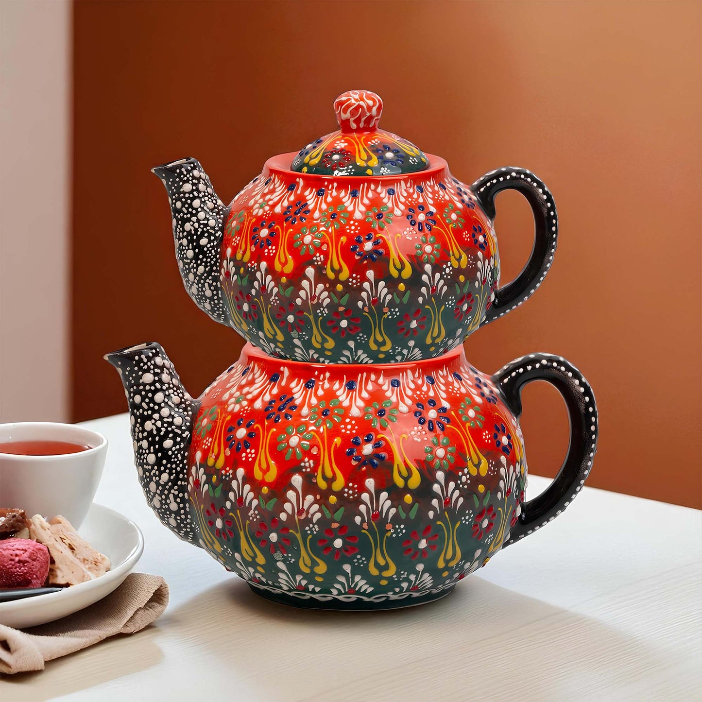 Decorative teapot with floral patterns on a table with a bowl of tea and cookies.