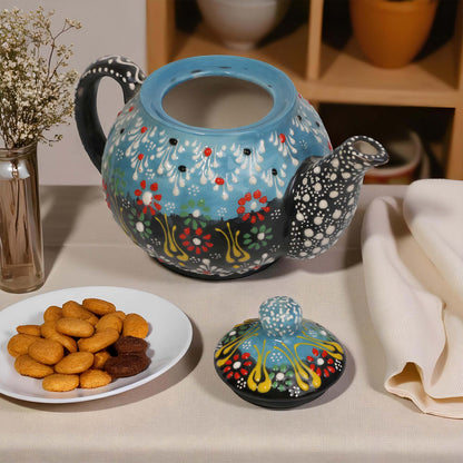 Decorative teapot with colorful floral pattern on a table with cookies and a vase.