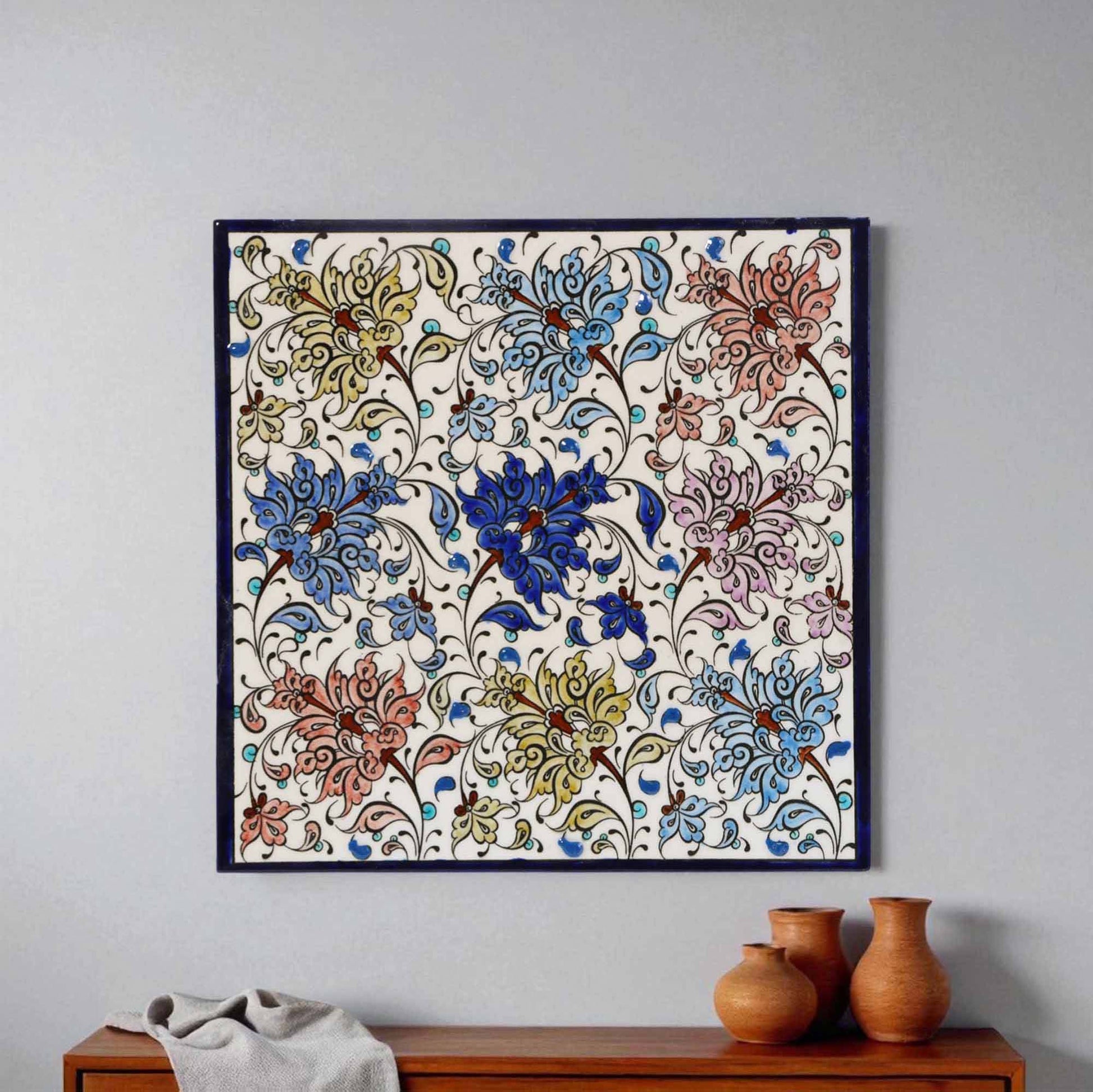 Decorative floral ceramic tile hanging on a wall above a wooden cabinet with vases.