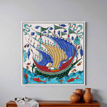 Decorative ceramic tile of a ship with colorful sails on a gray wall above a wooden cabinet.