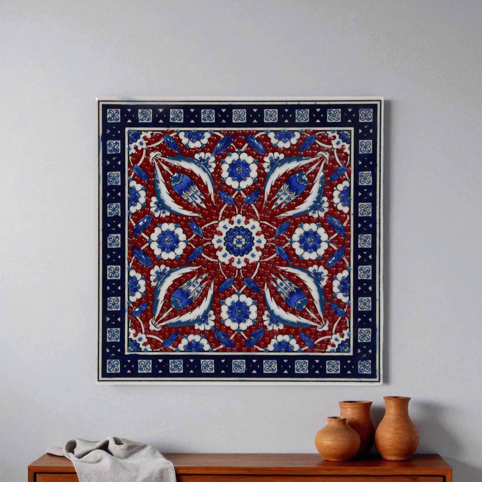 Decorative ceramic tile with a floral pattern in red, blue, and white on a plain wall above a wooden cabinet.