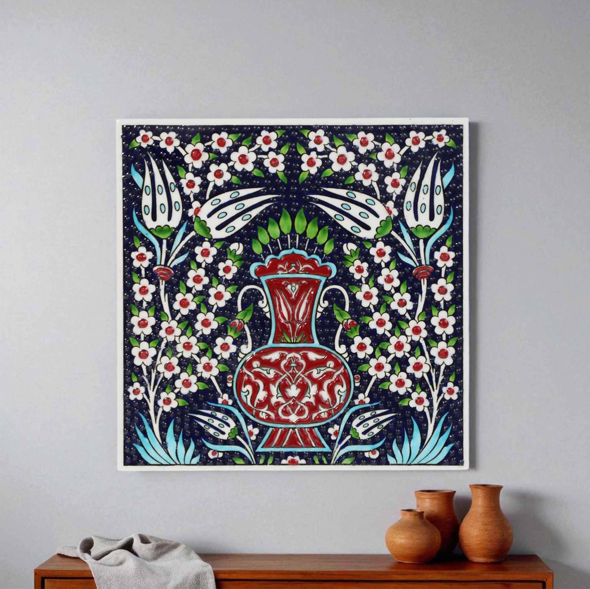 Decorative ceramic tile wall art with floral and vase design on a plain wall.
