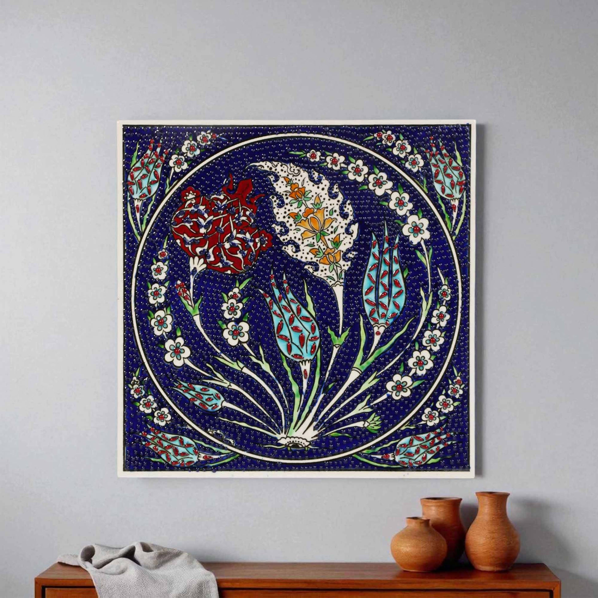 Decorative ceramic tile with floral design on a wall above a wooden cabinet.