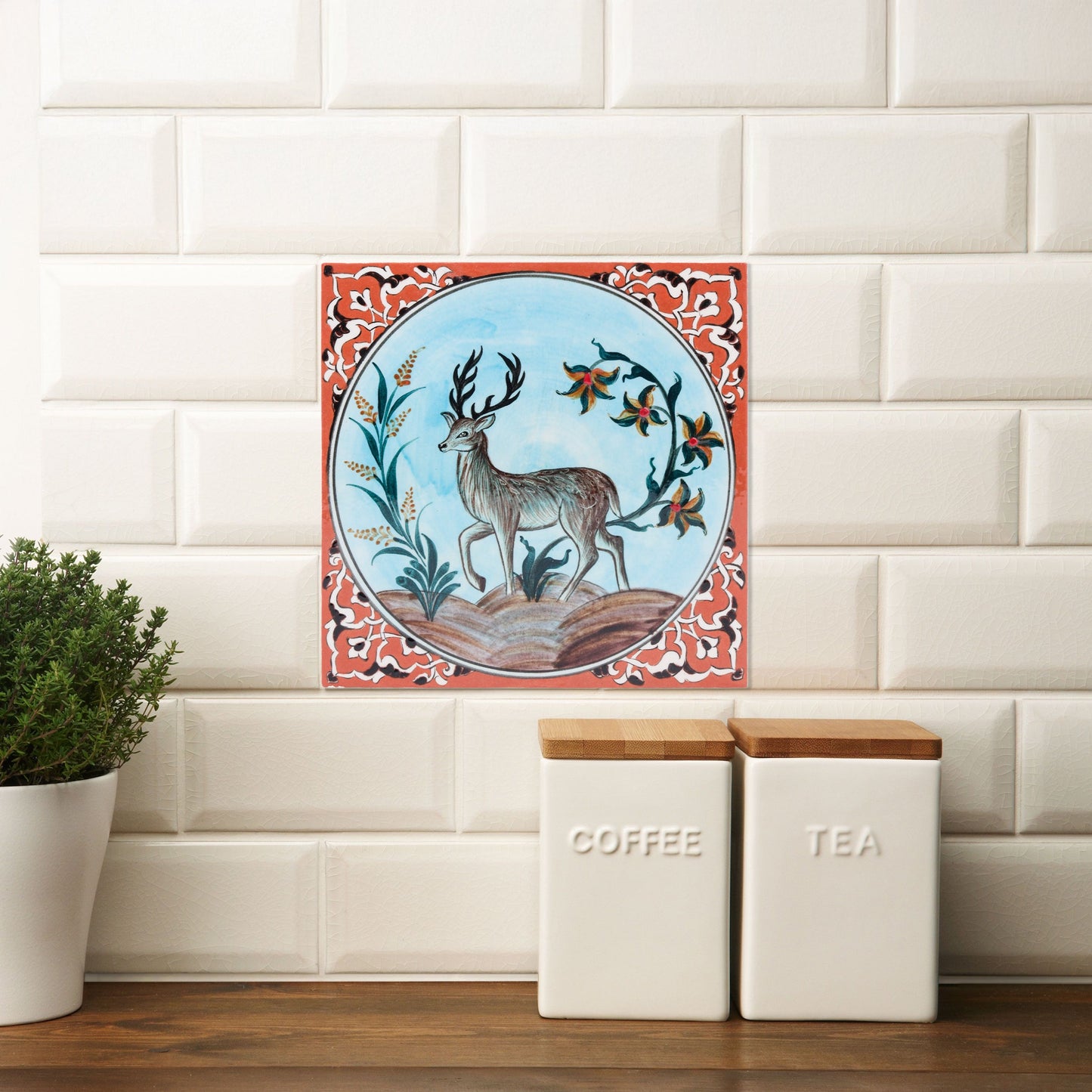 Decorative ceramic tile with deer design on a kitchen backsplash with coffee and tea canisters.