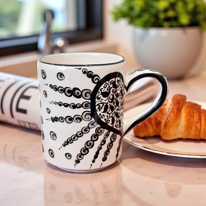 Mug with octopus design on a table with a croissant and newspaper