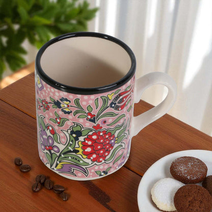 Decorative mug with floral pattern on a wooden table with cookies and coffee beans.