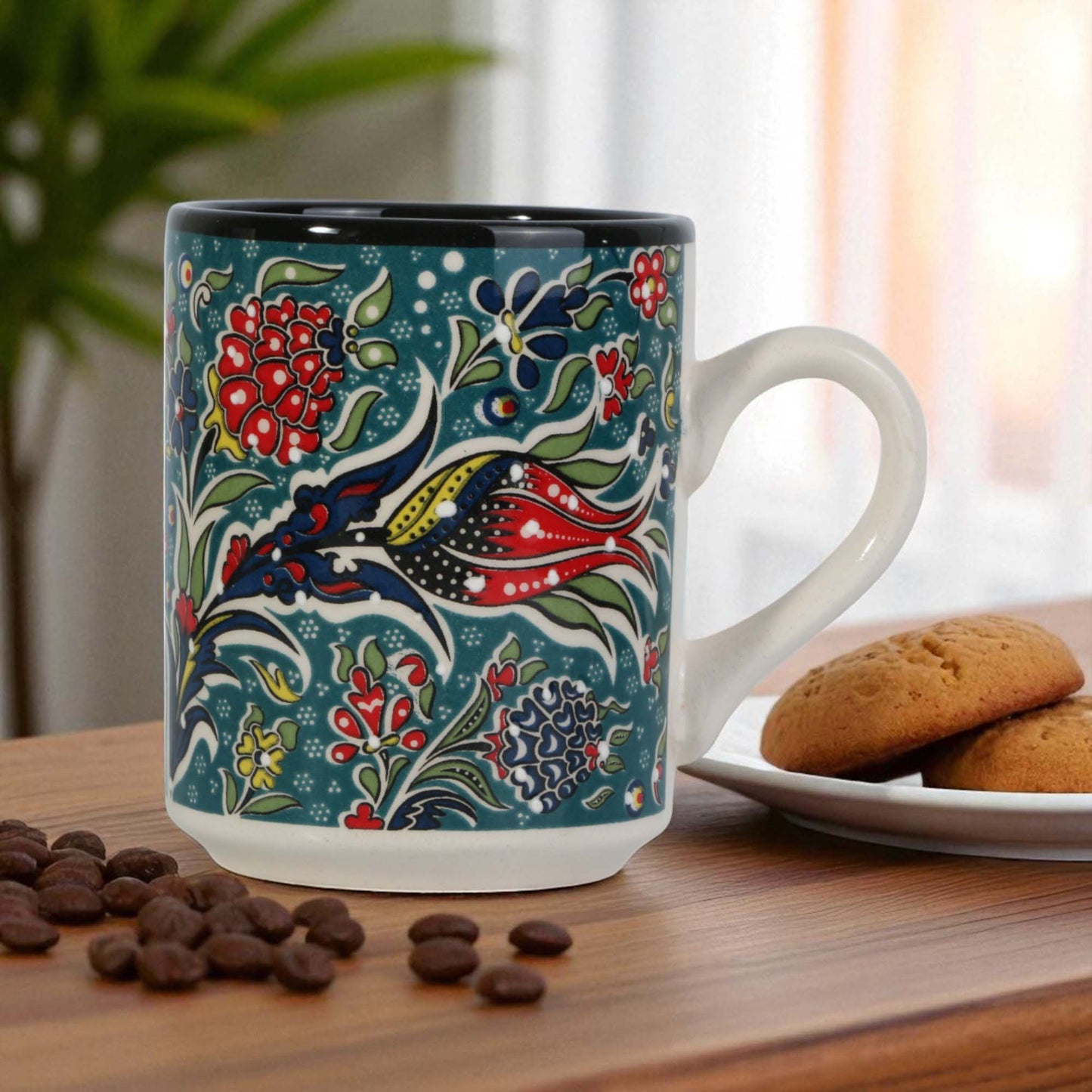 Decorative mug with floral pattern on a wooden table with cookies and coffee beans.