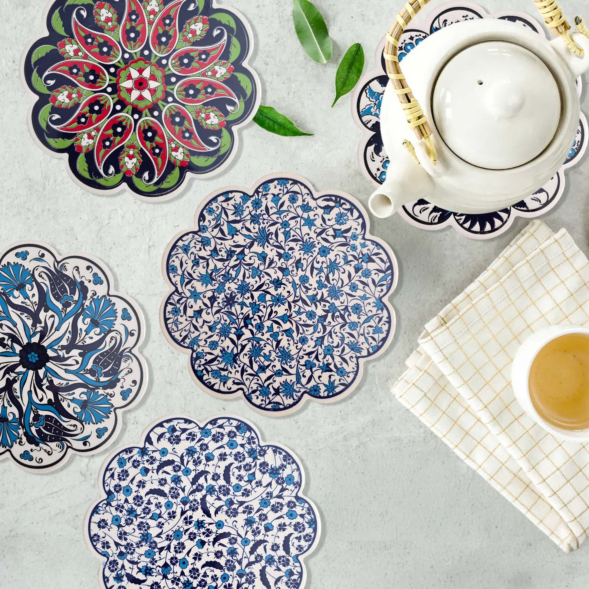 Decorative trivets with floral patterns on a table with a teapot and cup.