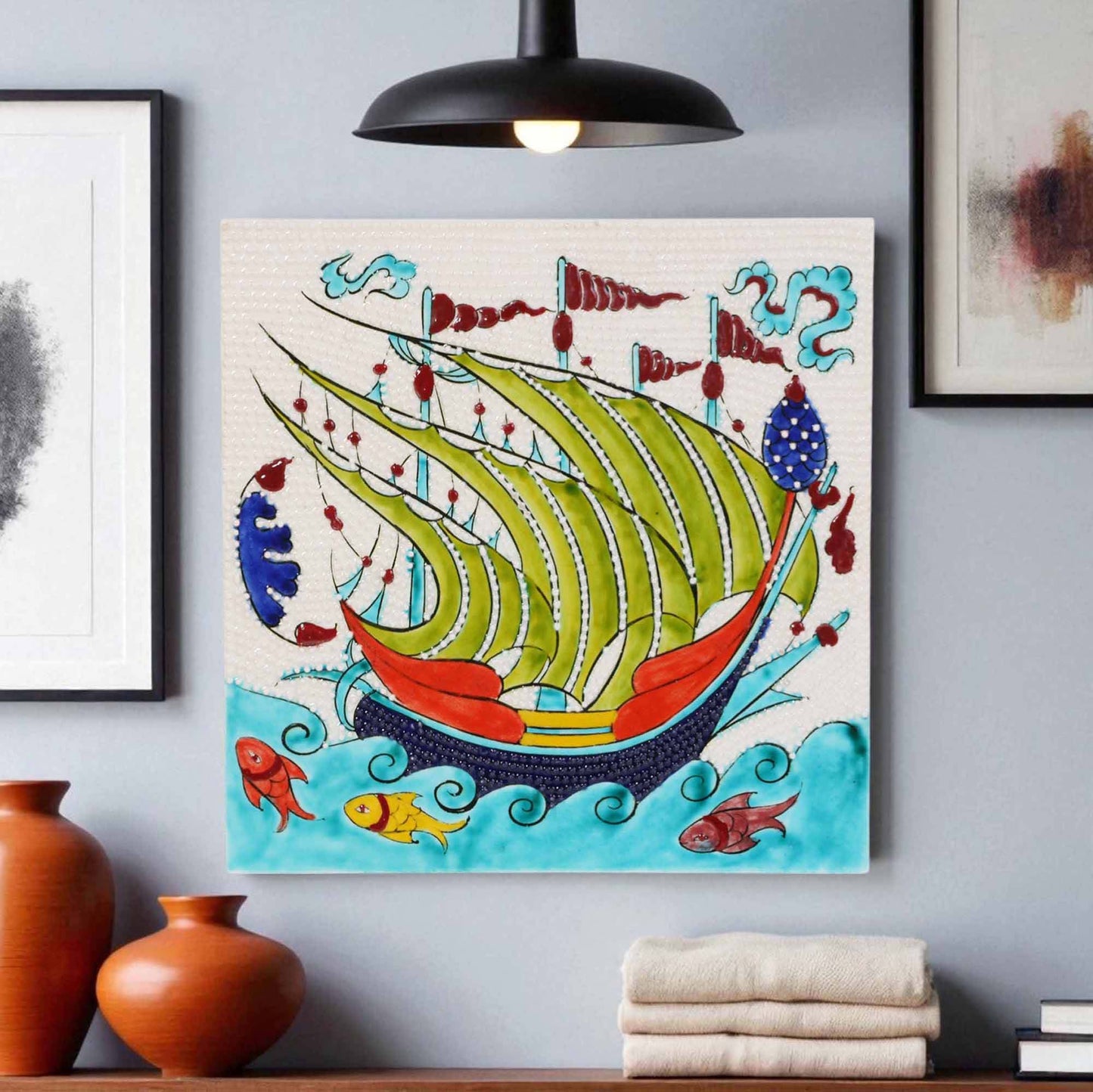 Colorful abstract ceramic tile of a ship on a wall with decorative vases and books below.