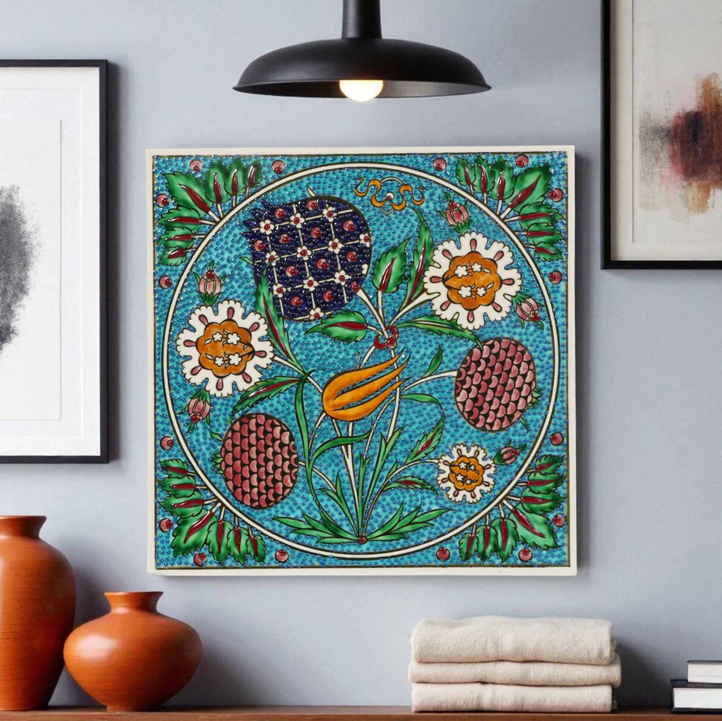 Decorative ceramic tile on a wall with vases and towels below.