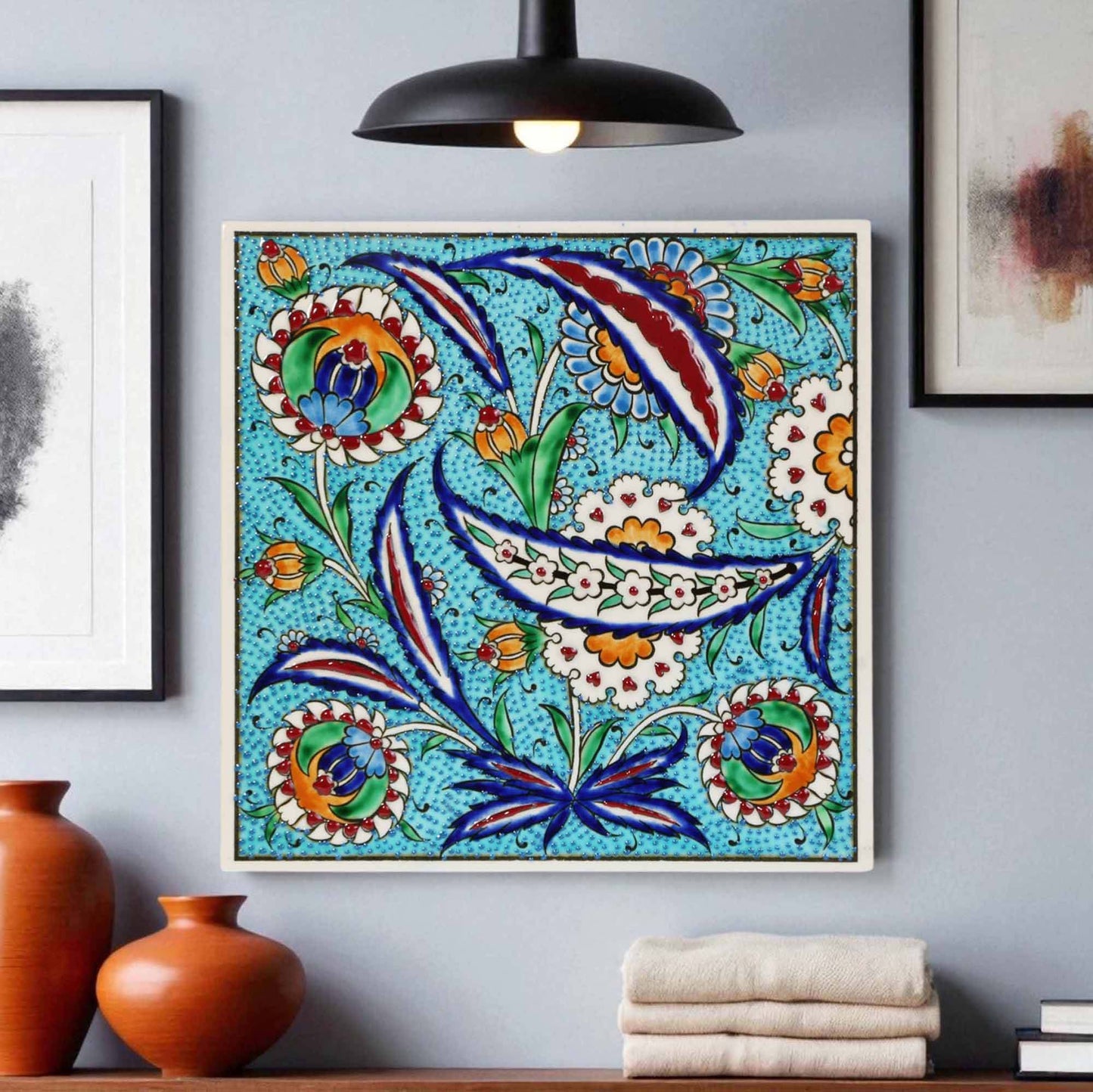 Decorative ceramic tile with floral patterns on a wall with vases and books below.