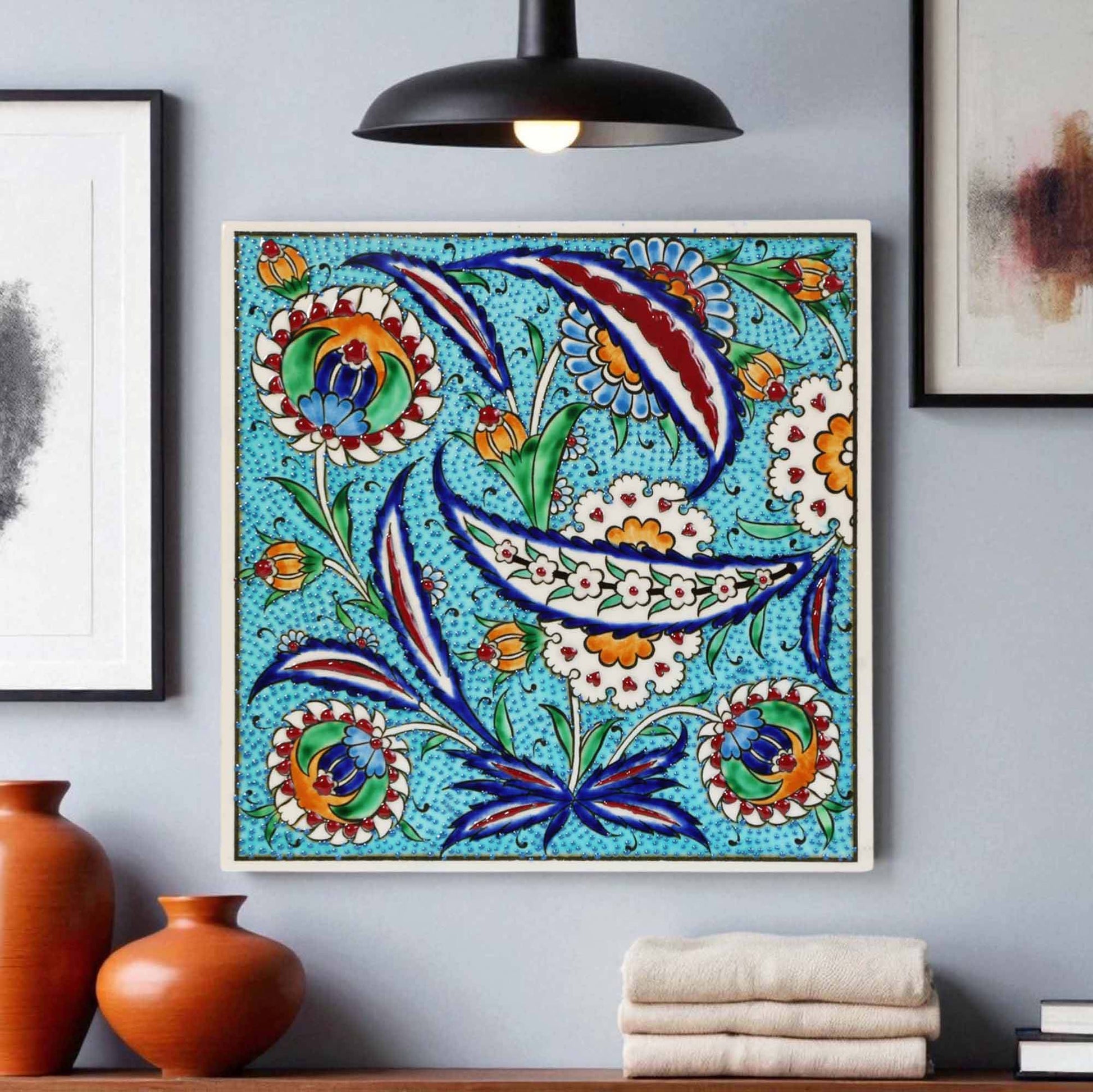 Decorative ceramic tile with floral patterns on a wall with vases and books below.