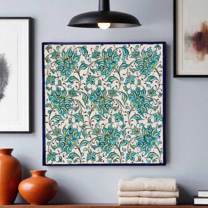 Decorative floral patterned ceramic tile on a gray wall with vases and books below.